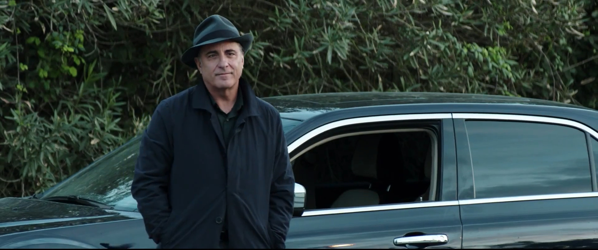 Andy Garcia con cappello accanto a un’auto nera