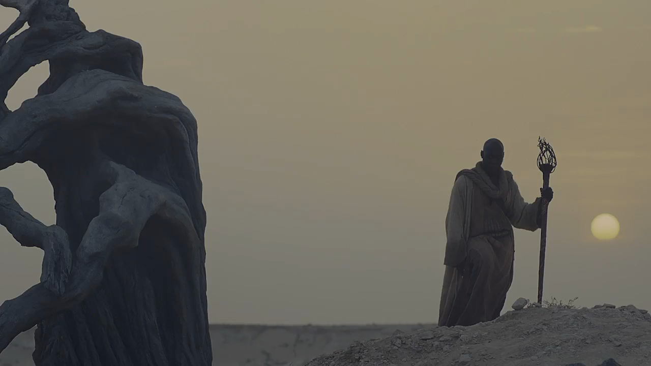 Figura con bastone nel deserto al tramonto